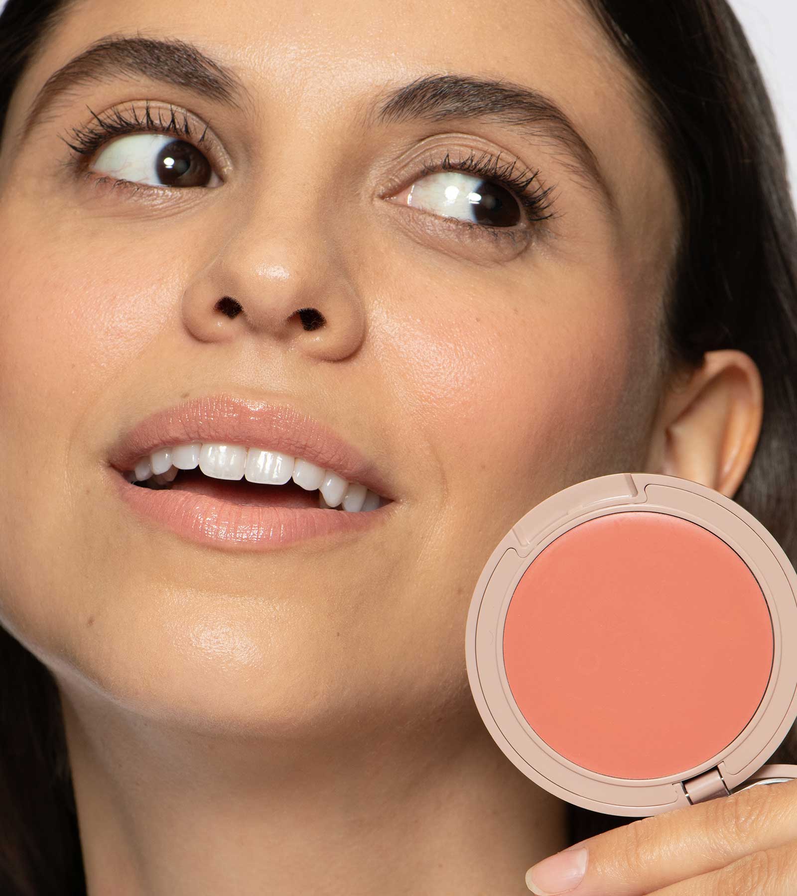Close-up of a woman's face with a compact peach blush palette next to her.