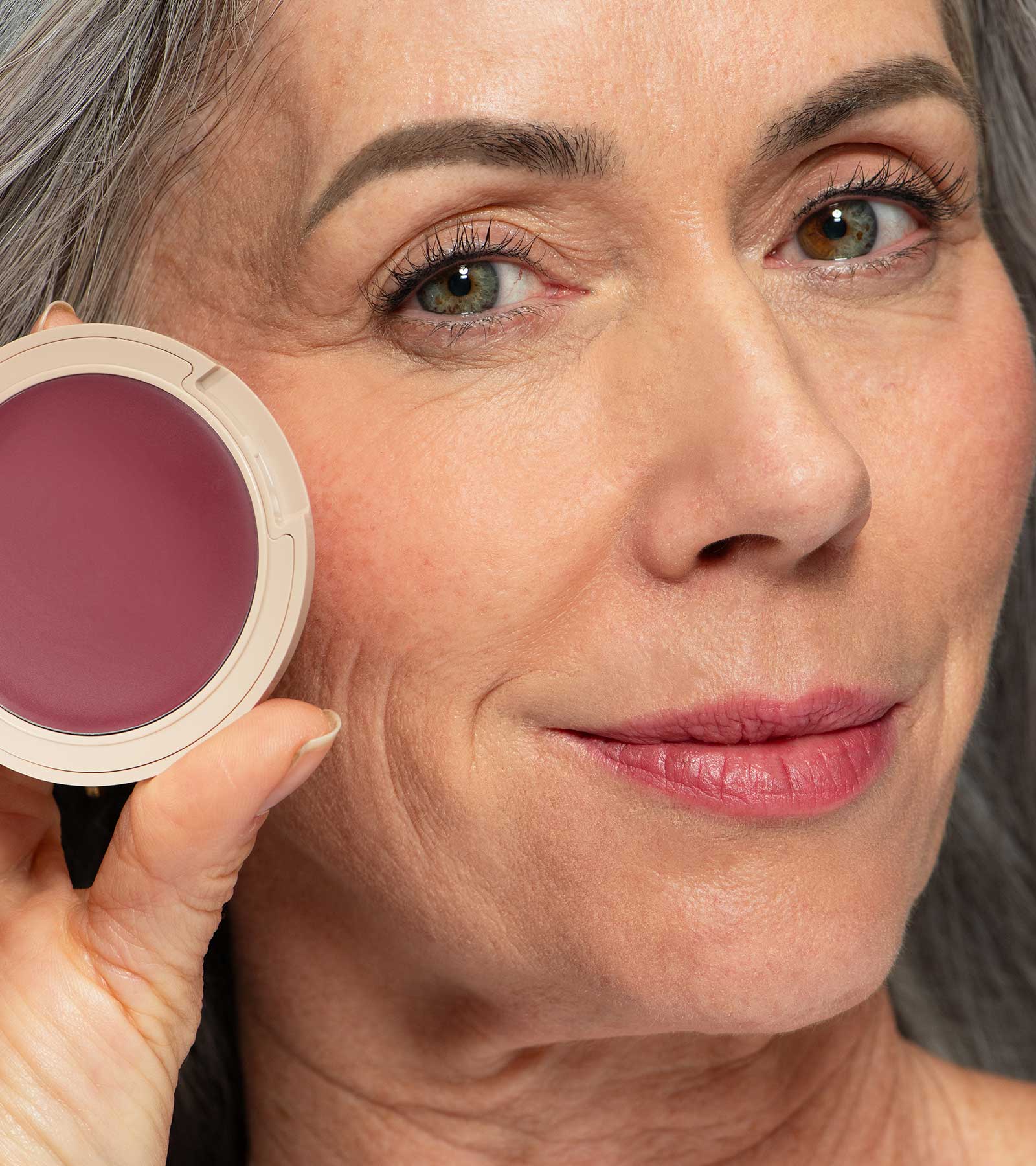 Close-up of a woman holding a plum blush compact