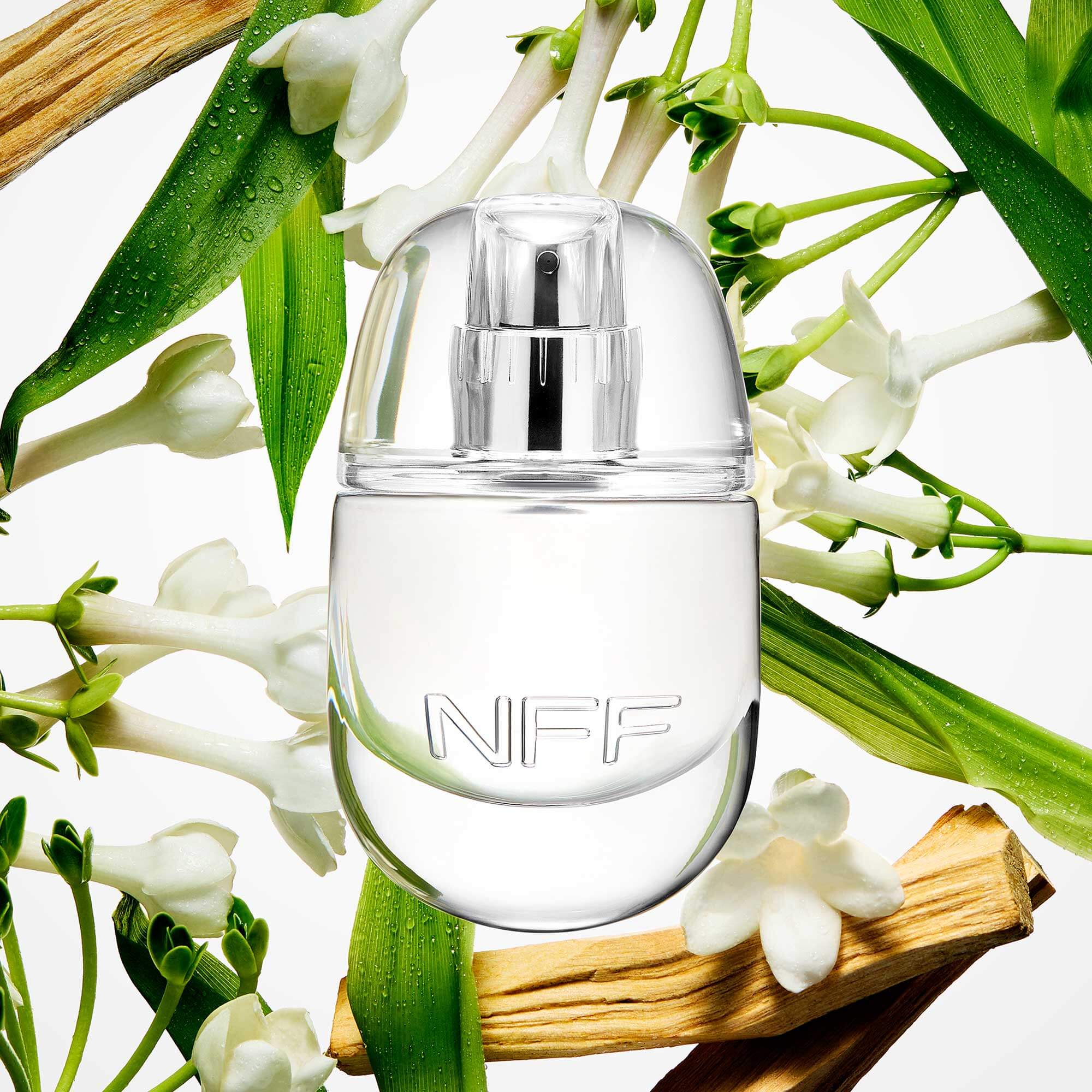 Clear NFF perfume bottle surrounded by white flowers and green leaves on a light background