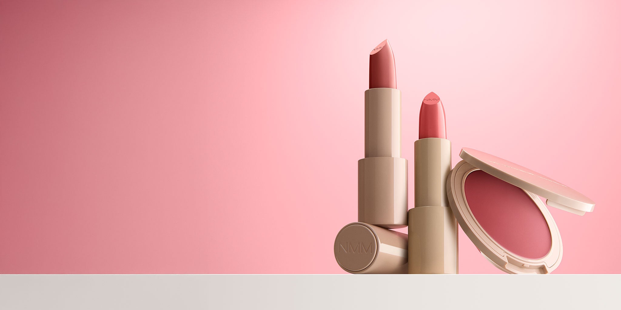 Makeup products including a lipstick, blush, and compact on a pink background