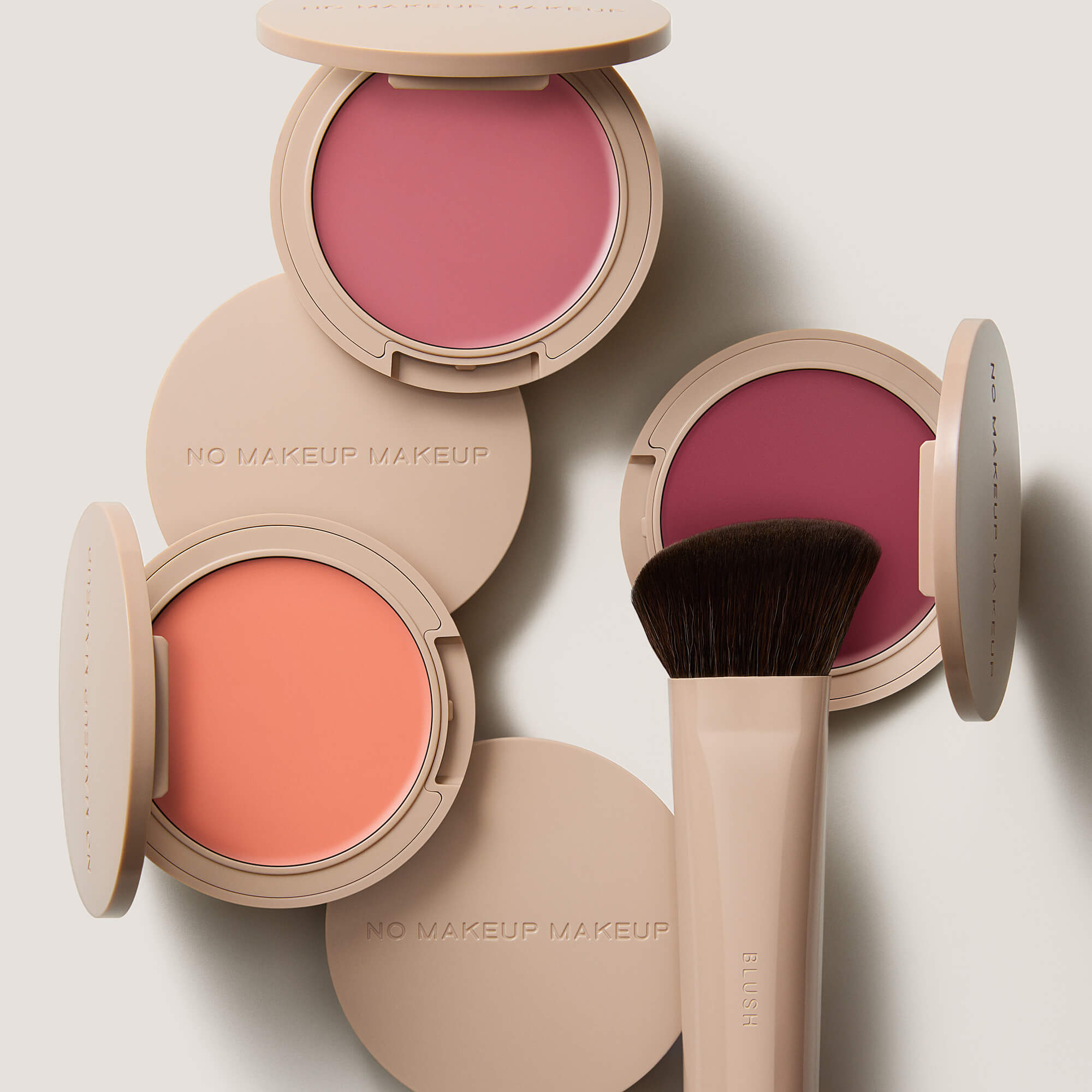No Makeup Makeup – Three open blush compacts in peach, pink, and plum shades and a brush, natural minimal makeup