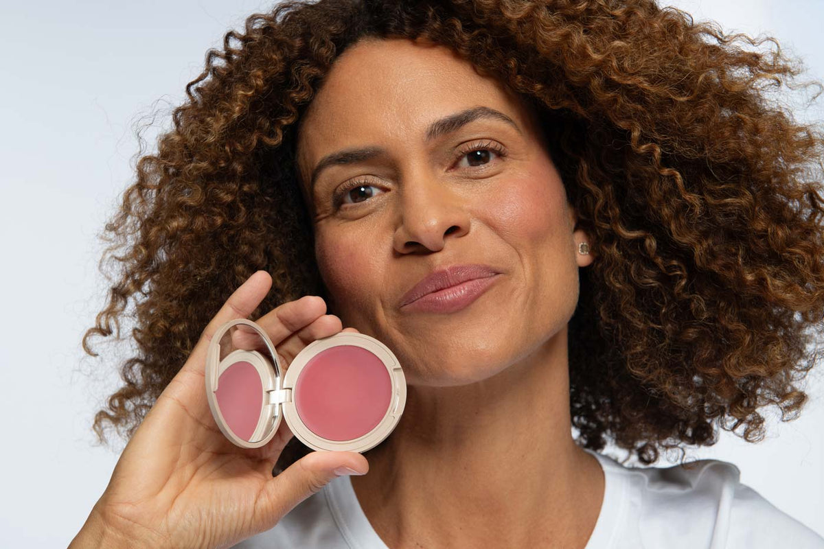 Woman with curly hair holding open No Makeup Makeup®'s 2-in-1 Blush & Lip product in the shade Pink.