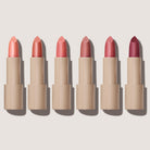 Six lipsticks with different shades of pink on a light beige background